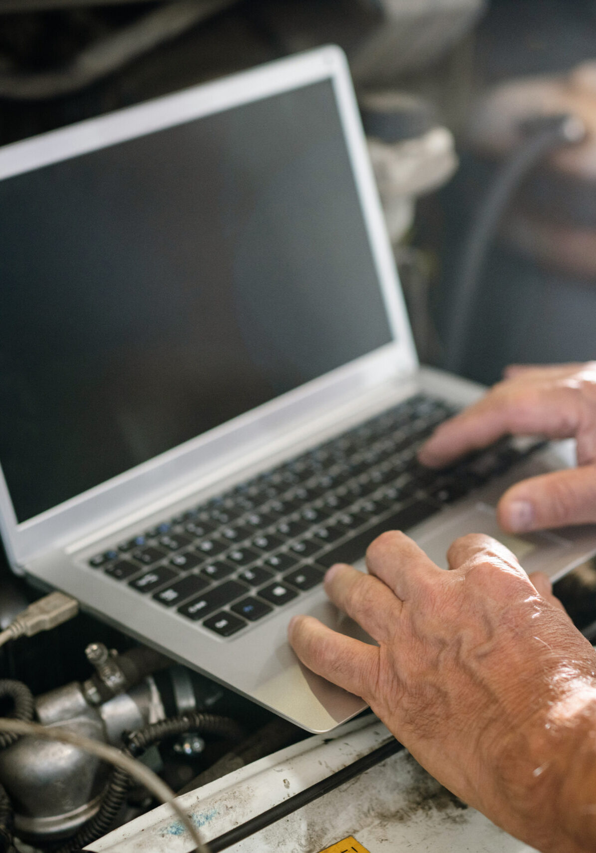 Hands of mature master of car repair service over keyboard of laptop during search of technical information